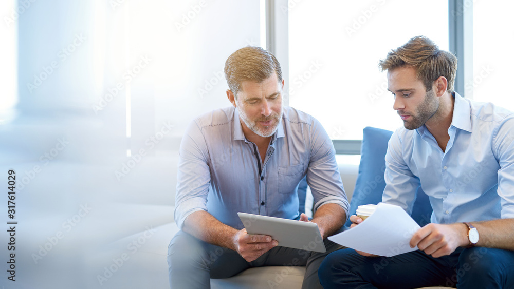 Mature businessman talking with younger colleague on couch - obrazy, fototapety, plakaty 
