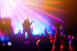 © maxbelchenko - Audience with hands raised at a music festival and lights streaming down from above the stage. Crowd raising their hands, dancing and enjoying great the concert.