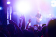 © maxbelchenko - Audience with hands raised at a music festival and lights streaming down from above the stage. Crowd raising their hands, dancing and enjoying great the concert.
