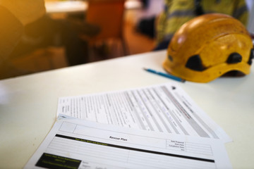 Defocused personal protective equipment safety helmet head protection placing on the table with working at height rescue plan paperwork at the foreground   