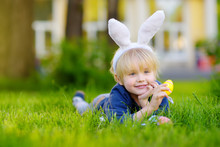 Pretty Little Boy Wearing Bunny Ears Hunting For Easter Eggs In Spring Park On Easter Day.