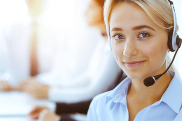 Group of diverse phone operators at work in sunny office. Handsome business woman with headphones consulting clients. Call center and business people concept