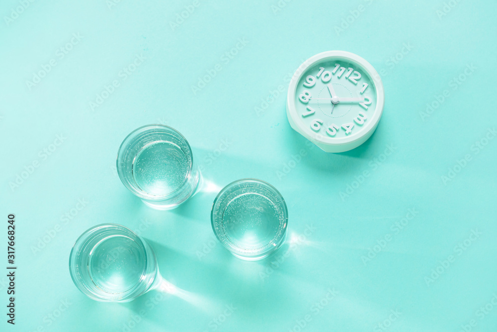 Glasses of clean water and clock on color background