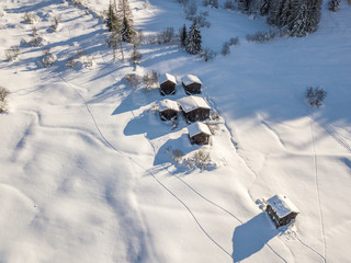 Wall Mural - Aerial view of snow covered cottages in wild rural countryside. Tranquil scene with beautiful wooden houses in remote mountain area.