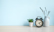 © Soho A studio - Empty blue wall and desk with alarm clock, home plant and ceramic vase. Copy space