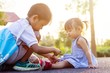 © waridsara - Soft focus. A young Asian brother help his little sister to tie her shoelaces. At the garden park in sunshine day summer season. Love and family concept.