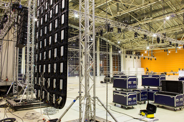 Spotlight devices on a trusses. Line array speakers. Big led screen. Flight cases. Installation of professional stage, sound, light and video equipment for a show.