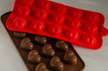 Two silicone molds for making homemade sweets. Red and brown molds for casting chocolate on a light background. Close-up. Selective focus. Landscape photo arrangement.