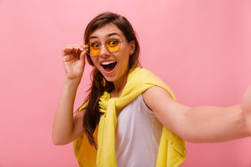 Wall Mural - Lovely asian girl posing with peace sign. Laughing asian young woman taking selfie on pink background. Positive emotions. Horizontal.