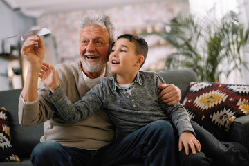 Grandfather teaching his grandson how to make paper airplane. Grandpa and grandchild playing together. 