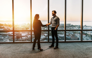 Smiling businesspeople shaking hands by office windows overlooking the city