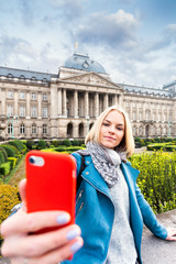 Wall Mural - A young woman stands in front of the royal palace in Brussels and takes a selfie on her phone, Belgium