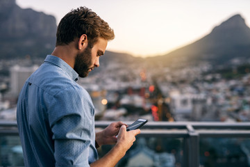 Wall Mural - Young businessman using a cellphone on an office balcony