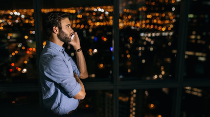 Wall Mural - Young businessman working late at night talking on a cellphone