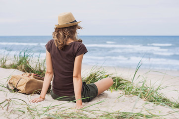 Wall Mural - Young woman resting by the sea. Girl sitting on the beach. Enjoying life, summer lifestyle, relaxation and travel concept