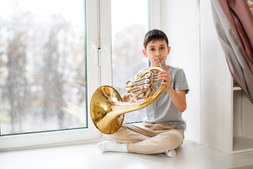 Caucasian boy learns to play horns, light window