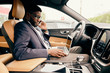 © Anton - Man talking on the phone during car ride with a laptop nearby.