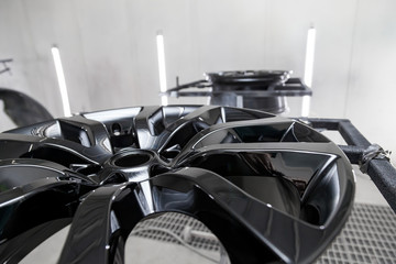 A Two black painted aluminum alloy wheel is mounted on a special frame during drying in a chamber in a vehicle body repair workshop. Auto service industry.