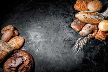 Assortment of fresh baked bread on dark background. White and rye bread, buns with copy place