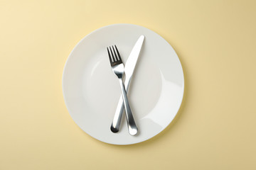 Plate with fork and knife on beige background, top view