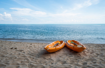 Two colorful orange kayaks on a sandy beach ready for paddlers in sunny day. Several orange recreational boats on the sand. Active tourism and water recreation.