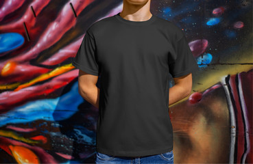 Wall Mural - Mockup black male t-shirt on a young guy against the background of a wall with graffiti, front view.