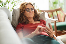 Smiling Mature Woman Lying On Her Couch Using A Cellphone