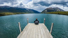 Man Sitting On Wooden Pier On A Lake