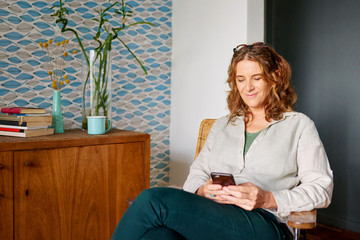 Wall Mural - Mature woman reading a text message while relaxing at home