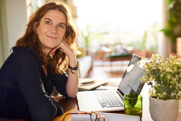 Wall Mural - Smiling mature female entrepreneur working at a table from home