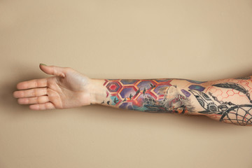 Wall Mural - Woman with colorful tattoos on arm against beige background, closeup