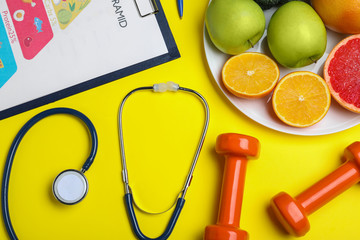 Wall Mural - Fruits, dumbbells, stethoscope and list of products on yellow background, flat lay. Visiting nutritionist