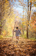 © Cavan Images - Young boy walking on leaf covered path with a big stick on autumn day.