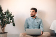 © Cavan Images - Man using laptop computer while sitting against wall on floor at home