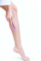 Closeup of slender female foot on white background. Young woman is shaving her leg with pink disposable razor. Tool to remove unwanted body hair, personal care product. Depilation concept.