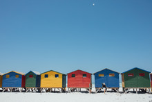 Women Walking By Beach Huts Against Clear Blue Sky