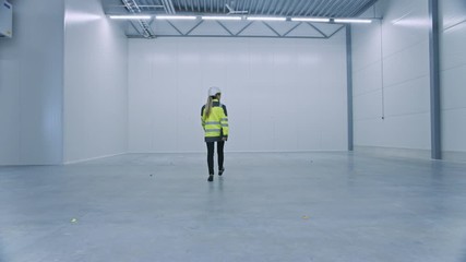 Poster - Female Engineer Wearing Safety Hat Walks Across Empty Factory Floor, Inspecting, Planning Where Machinery Would go. Professional Industrial Designer Strategizing about New Manufacturing Plant Design