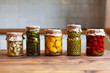 Pickled patissons, cucumbers, mushrooms, green pea and tomatoes canned into glass jars. Ingredients for vegetables preserving. Healthy fermented food concept. Harvest storing. Fermented vegetables