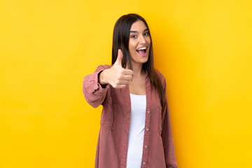 Wall Mural - Young brunette woman over isolated yellow background with thumbs up because something good has happened