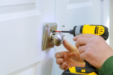 Wall Mural - Handyman using a drill to installing lock in door in a house