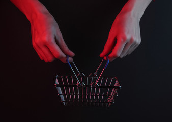 Wall Mural - Female hands holding a shopping basket on a black background with red neon light