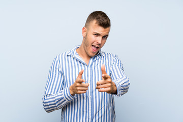 Wall Mural - Young handsome blonde man over isolated blue background pointing to the front and smiling