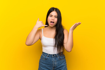 Wall Mural - Young teenager Asian girl over isolated yellow background making phone gesture and doubting