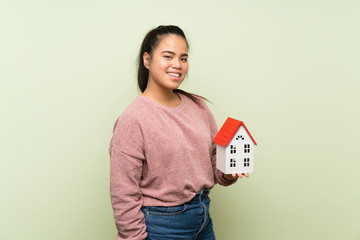 Wall Mural - Young teenager Asian girl over isolated green background holding a little house