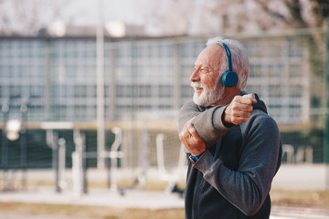 Wall Mural - An elderly man stretching his shoulder in an outdoor sports centre.