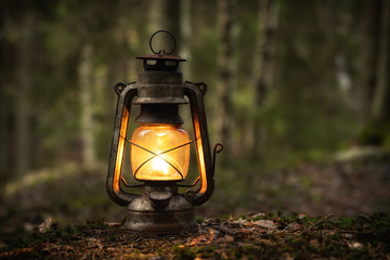 vintage old lantern lighting in the dark forest. travel camping concept. burning lantern on a moss a