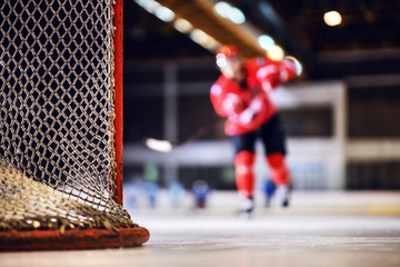 Close up of goal. In background is hockey player skating towards goal and shooting at it.