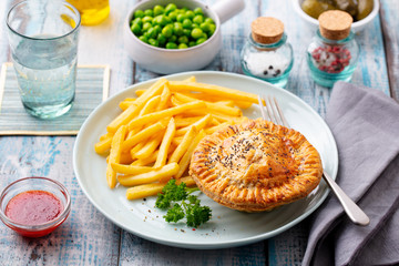 Wall Mural - Meat pie with french fries on a white plate. Wooden background. Close up.