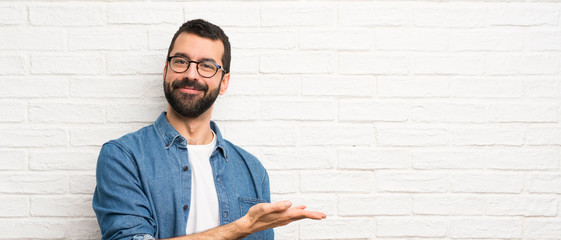 handsome man with beard over white brick wall presenting an idea while looking smiling towards