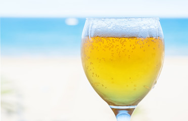 Glass of beer with foam and bubbles on background of blue sky and sea